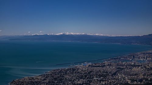 Aerial view of sea by city against blue sky