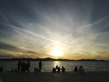 Silhouette people on beach against sky during sunset