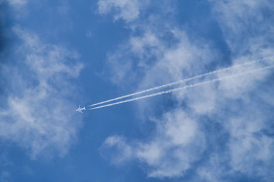 Low angle view of airplane and vapor trail against blue cloudy sky