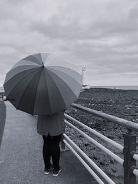 Rear view of woman standing on railing against sea during rainy season