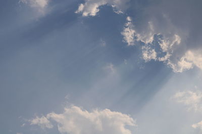 Low angle view of sunlight streaming through clouds