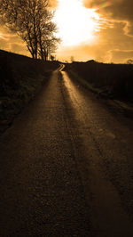 Dirt road along trees on landscape against sunset sky