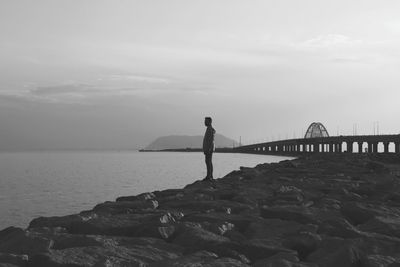 Man standing on rock by sea against sky