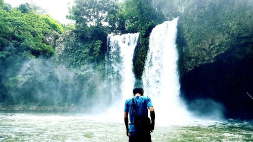 Man standing by waterfall in forest