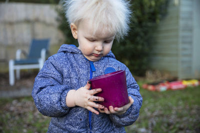 Cute boy holding flower pot while standing outdoors