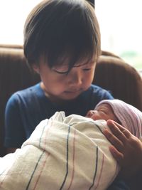 Cute boy carrying wrapped baby girl at home