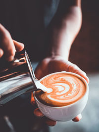 Midsection of barista pouring milk in coffee at cafe