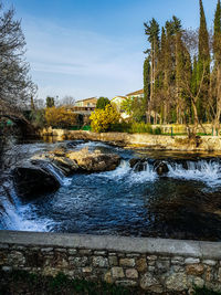 River flowing by trees against sky