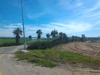 Road passing through field against cloudy sky