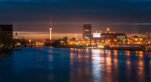 Illuminated city at waterfront during sunset
