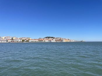 Sea by townscape against clear blue sky