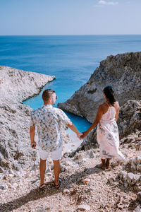 Rear view of couple standing on rock by sea against sky