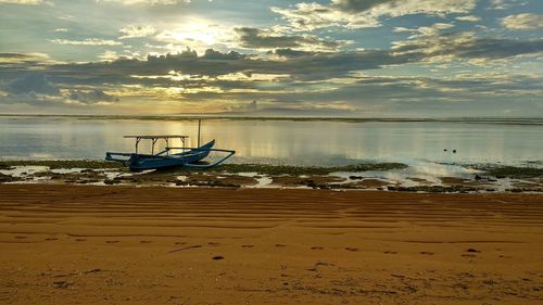 Boat moored on beach against sky during sunset