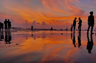 Silhouette people on beach against sky during sunset