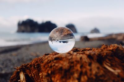 Close-up of crystal ball on beach against sky