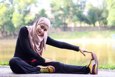 Portrait of mid adult woman wearing hijab while exercising by lake at park