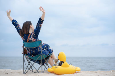 Woman relax and sit on beach chair with her cat sit on duck rubber ring on sand beach