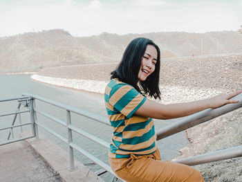 Portrait of smiling young woman standing by railing on steps