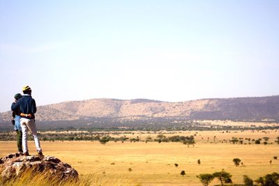 Rear view of couple standing on rock against clear sky