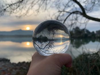 Midsection of person holding crystal ball against lake