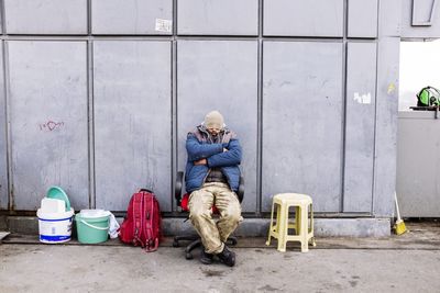 Man relaxing on chair at sidewalk against wall