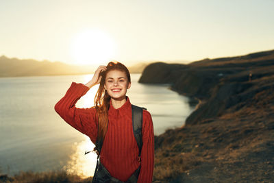 Portrait of smiling young woman standing in sea against sky