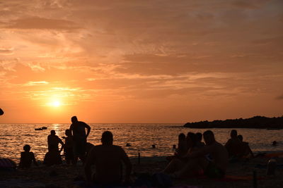 Silhouette people on beach against sky during sunset