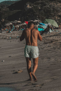 Rear view of shirtless man standing on beach