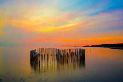 Wooden posts in sea against romantic sky at sunset