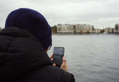 Close-up of man photographing river with smart phone in city