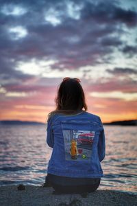 Rear view of woman looking at sea against sky during sunset