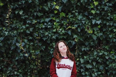 Portrait of young woman standing against plants at park