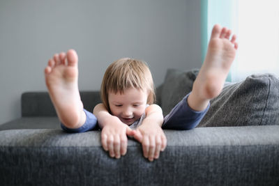 Child jumps and plays on sofa in minimalist living room, gray sofa.