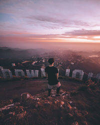 Rear view of man looking at cityscape against sky during sunset