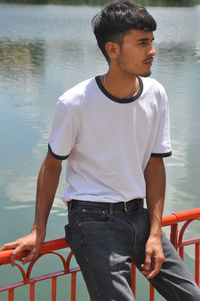 A handsome indian young guy wearing white t-shirt and black jeans, posing by lake and looking away