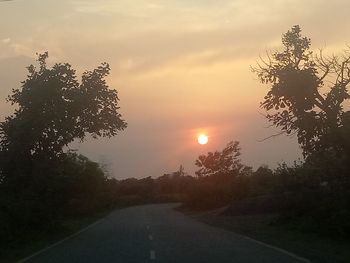 Road amidst trees against sky during sunset