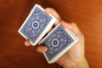Cropped hands of person holding playing cards on wooden table