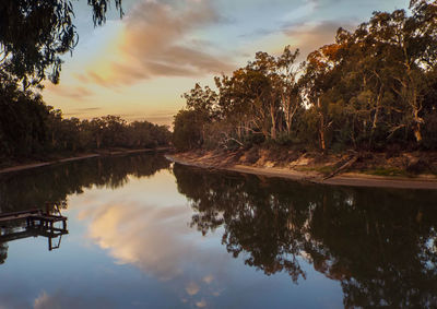 Reflection of silhouette trees in lake against sky during sunset