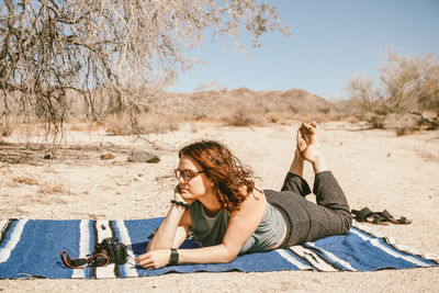 Young woman lying down on sand at beach against sky