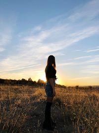 Side view of woman standing on field against sky during sunset