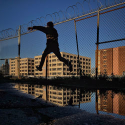 Silhouette man jumping by lake against sky in city