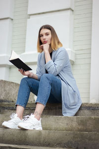 Low angle view of young woman reading book while sitting on sofa