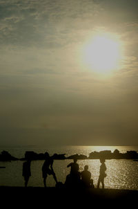 Silhouette people standing by sea against sky during sunset