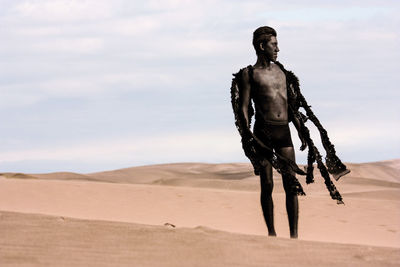 Teenage boy in costume on desert against sky