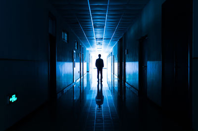 Rear view of silhouette woman walking in illuminated corridor