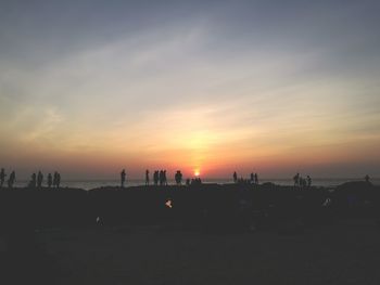 Silhouette people on beach against sky during sunset