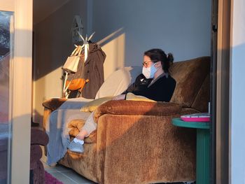 Woman wearing mask sitting on sofa at home