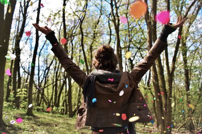 Rear view of woman enjoying with confetti on woodland