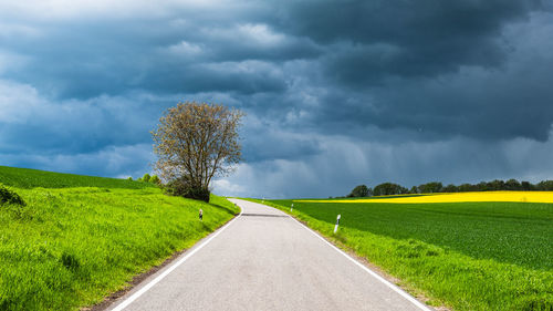 Road reaching out to storm surrounded by fields