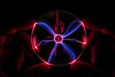 Cropped hands of person holding illuminated crystal ball against black background